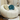A round, bubble-style upholstered accent chair in off-white velvet, styled with two round throw pillows in beige faux fur and teal velvet. The chair is set in a decorated room with beige curtains, a white side table, and a decorative ceramic vase.