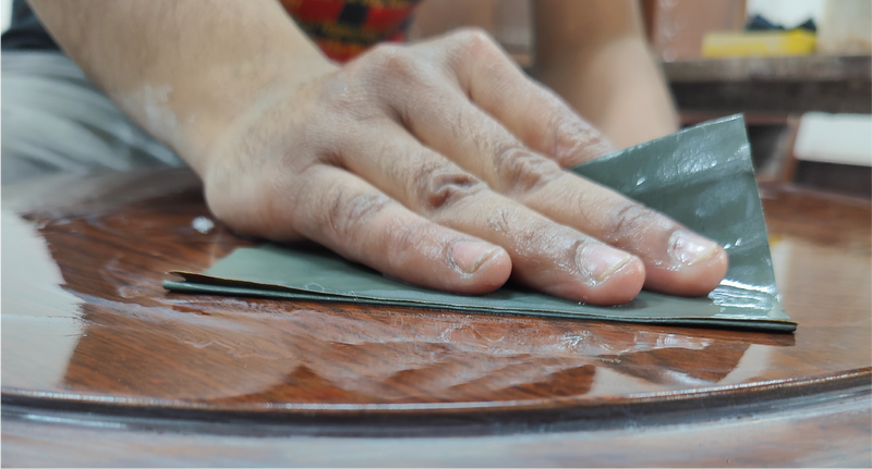Hand using a green cloth to polish a wooden surface
